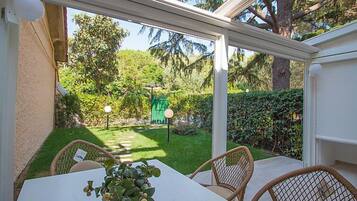 A conservatory with a view of a well-maintained garden, a table with chairs, and a potted plant.