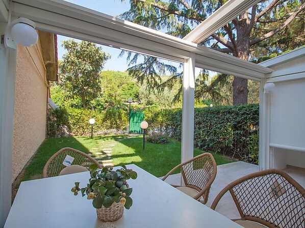 A conservatory with a view of a well-maintained garden, a table with chairs, and a potted plant.