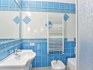 Un baño con azulejos azules, un lavamanos blanco, un bidé y un perchero para toallas.