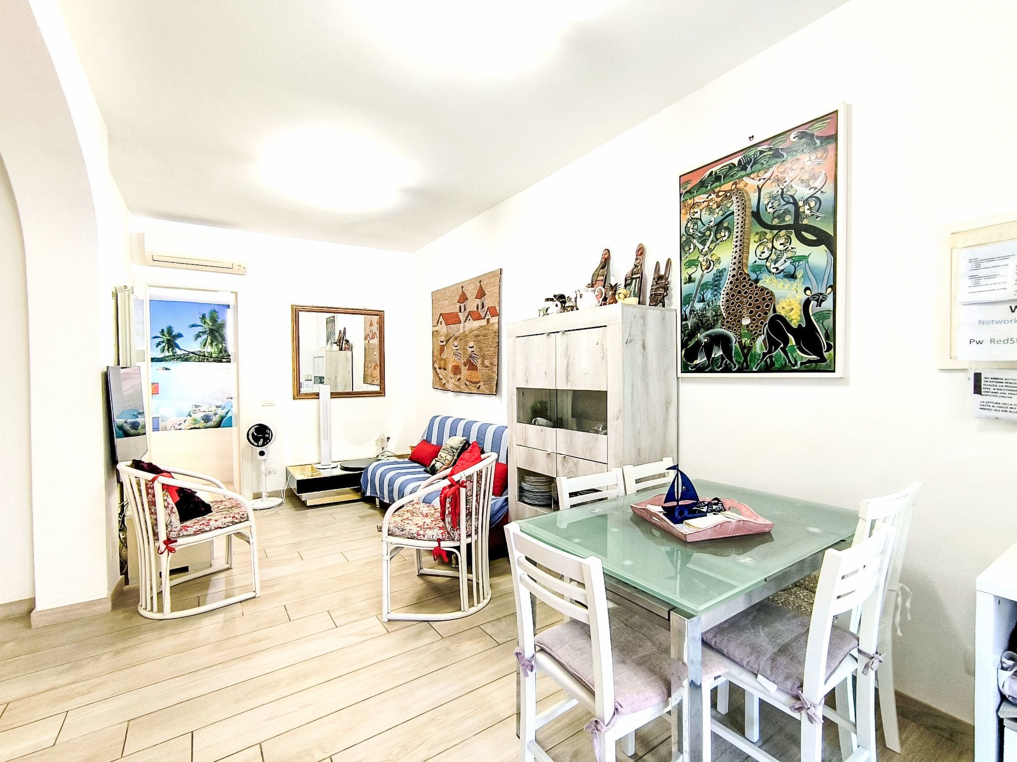 A room with a dining table, chairs, a sofa, a TV, and artwork on the walls.
