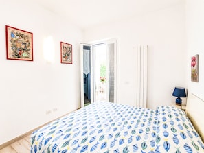 Una camera da letto con un letto, una porta che dà su un balcone e due quadri appesi al muro.