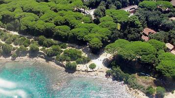 An aerial view of a coastal area with dense green trees, a sandy beach, and clear turquoise waters.