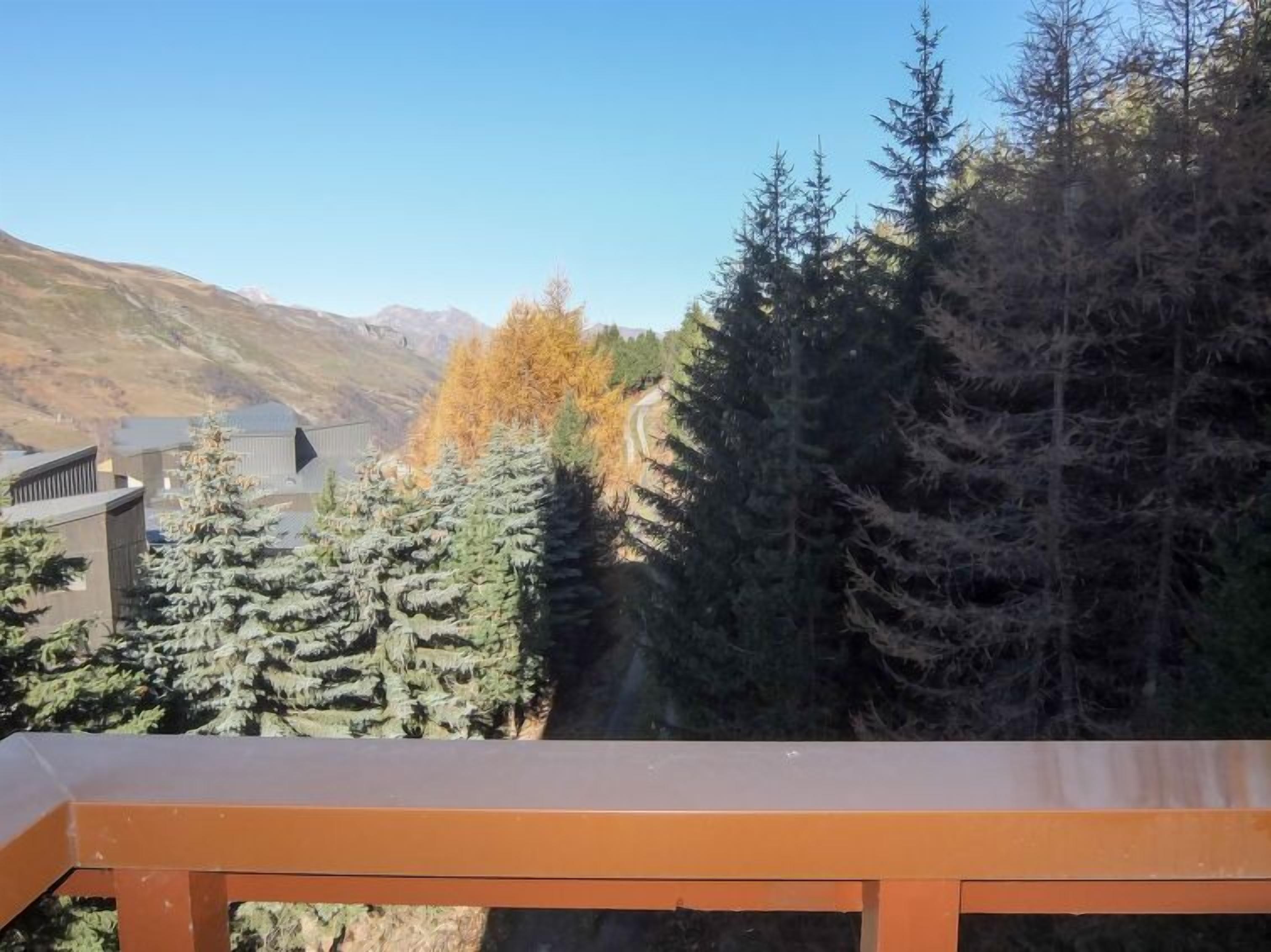 A view from a balcony overlooking a mountainous landscape with evergreen trees and a building in the background.
