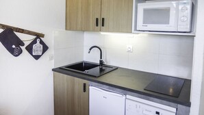 Une cuisine compacte avec des meubles en bois, un évier noir, un lave-vaisselle blanc et deux micro-ondes.