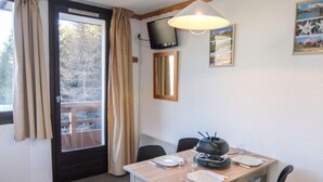Un coin repas avec une table dressée pour deux personnes, un téléviseur fixé au mur et une fenêtre avec des rideaux.