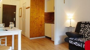 Ein kompakter Wohnraum mit Esstisch, einem schwarz-weißen Sofas und Holzabtrennung sowie einer kleinen Küchenzeile.