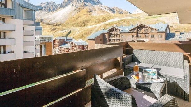 A balcony with wicker furniture, a table with a tray, and a mountain view. - Le Pramecou (Val Claret) by Interhome (Tignes)