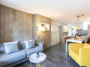 A modern living room with a grey sofa, a yellow armchair, and a dining area with a table set for two.