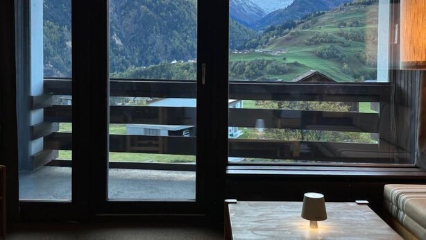 Ein Zimmer mit großem Fenster und Blick auf eine gebirgige Landschaft.