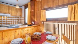 Ein Holzinterieur mit Küchenzeile, Esstisch gedeckt mit Tellern, Gläsern und einem Korb mit Brot.