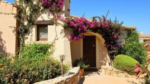 A building with a stone wall entrance, a wooden door, and a window. - Corbezzolo 11 - Vista Village by Interhome (Porto San Paolo)