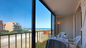 Een balkon met een tafel voor twee, met uitzicht op een strand en gebouwen.