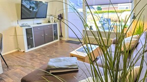 A living room with a sofa, a television, and a window with a view of a building. - Ankerweg by Interhome (Norddeich)