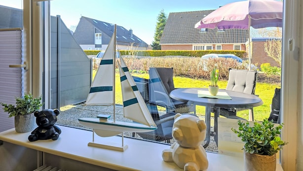 A room with a large window, a sailboat model, a teddy bear, and a table with chairs. - Ankerweg by Interhome (Norddeich)