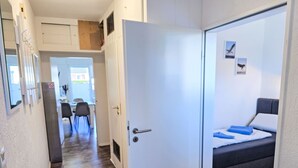 A hallway leading to a bedroom with a bed, a desk, and chairs in the background. - Ankerweg by Interhome (Norddeich)