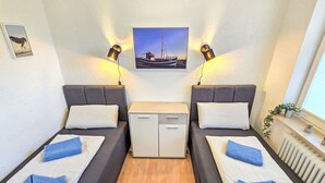 A twin room with two beds, a small table, a radiator, and a framed picture on the wall. - Ankerweg by Interhome (Norddeich)
