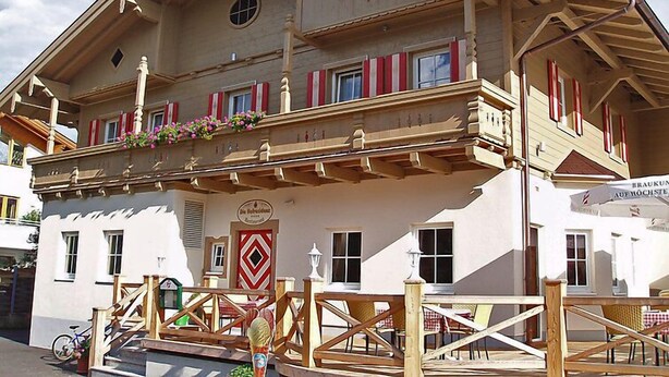 Un edificio de estilo alpino tradicional con balcón, barandillas de madera y contraventanas rojas.