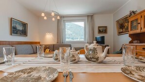 Un coin repas avec une table dressée pour deux personnes, une théière et un téléviseur en arrière-plan.