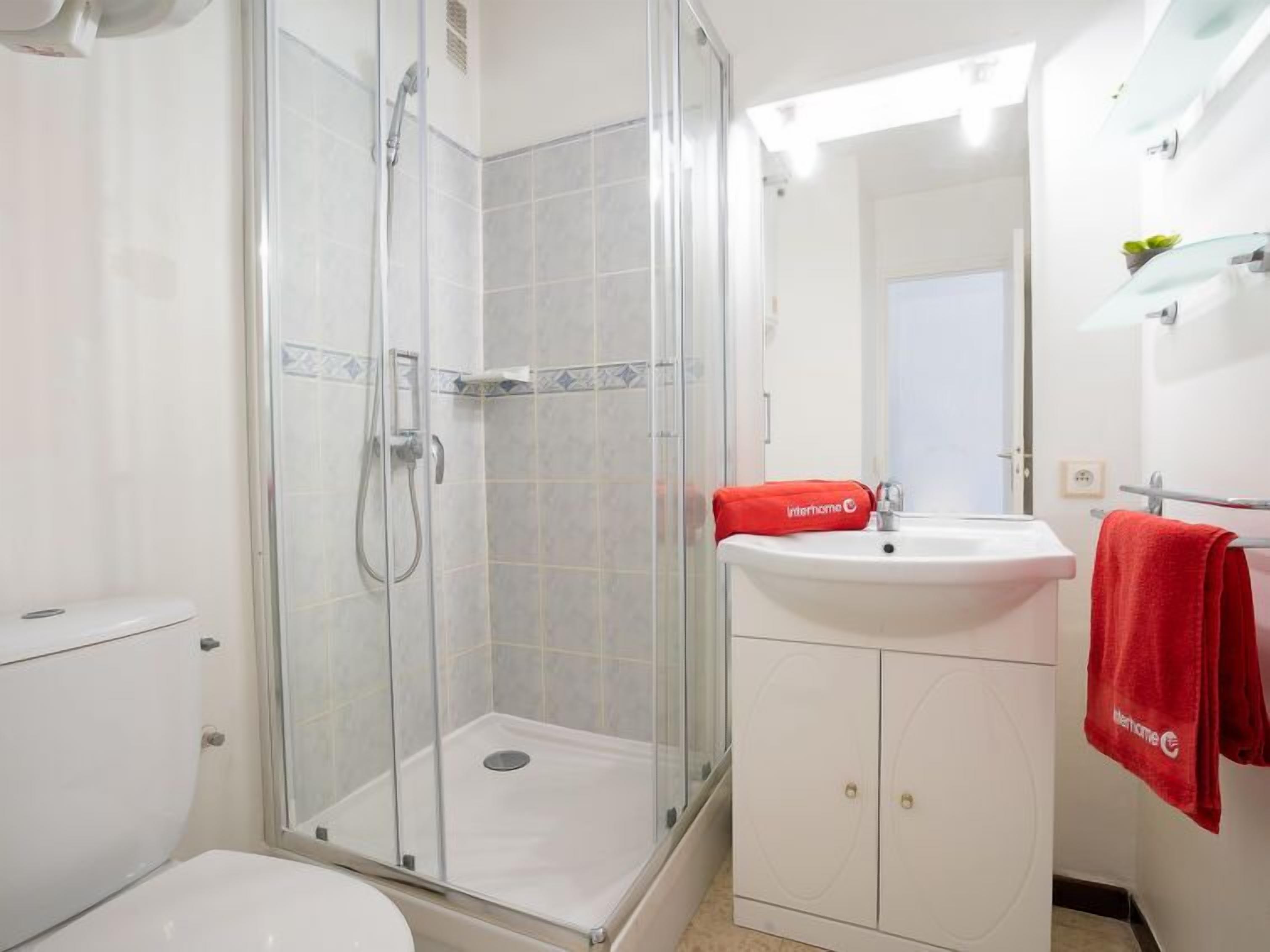 A bathroom with a glass-enclosed shower, a white sink with a red towel, and a white cabinet.