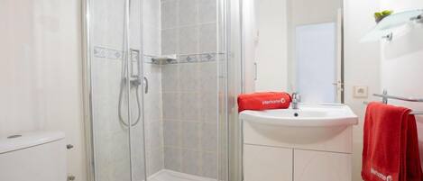 A bathroom with a glass-enclosed shower, a white sink with a red towel, and a white cabinet.