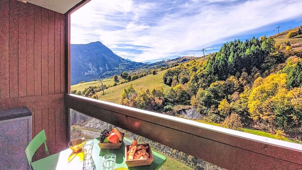 A balcony with a table set for two, overlooking a mountainous landscape with autumn foliage. - Vostok Zodiaque by Interhome (Le Corbier)
