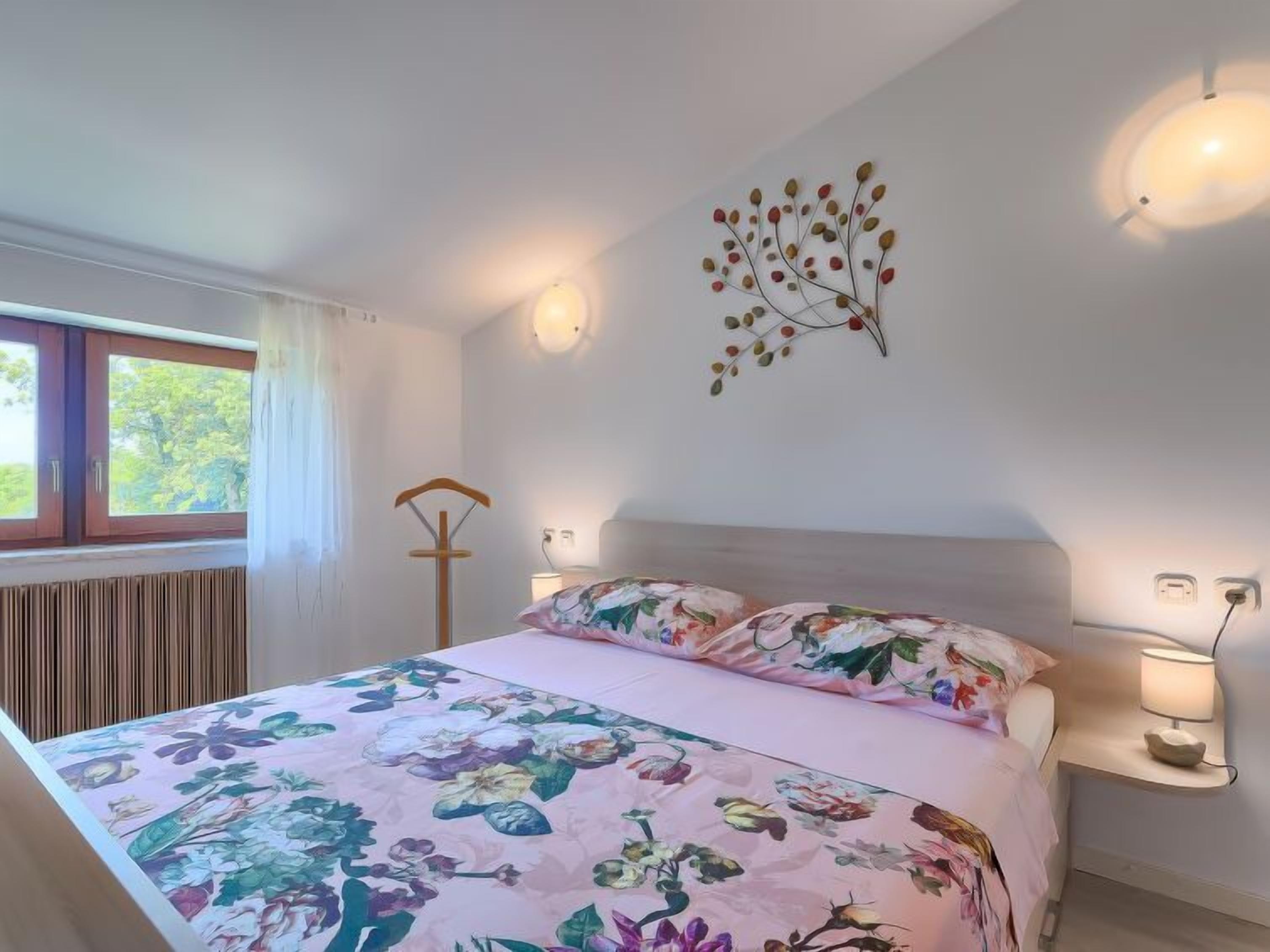 A bedroom with a floral bedspread, a bedside lamp, a wall-mounted light, and a radiator.