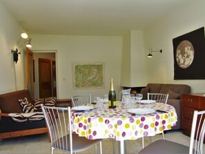 A dining area with a round table covered by a polka dot tablecloth, surrounded by white chairs. There is a bottle of champagne on the table, and a painting is visible on the wall.