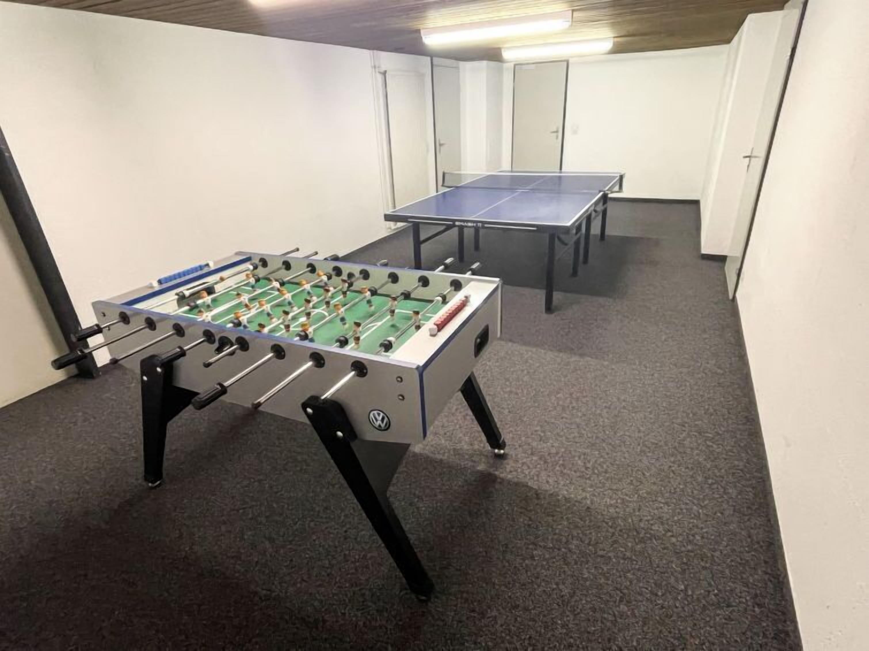 A room with two foosball tables, carpeted floor, and white walls.