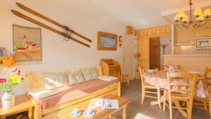 Ein gemütliches Wohnzimmer mit einer Couch, einem Couchtisch und einem Essbereich mit Stühlen und Tisch. An der Wand hängen Ski und über der Couch hängt ein Gemälde.
