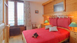 Ein Schlafzimmer mit einem hölzernen Kopfteil, einem Bett mit roter Bettdecke, zwei Nachttischlampen und einem Fenster mit Vorhängen.