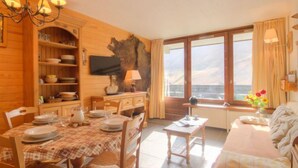 Ein gemütliches Zimmer mit Esstisch für vier Personen, einer Couch, einem Fernseher und einem großen Fenster mit Aussicht.