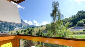 Un balcon avec une table et des chaises, donnant sur un paysage montagneux parsem é d’arbres et sous un ciel dégagé.