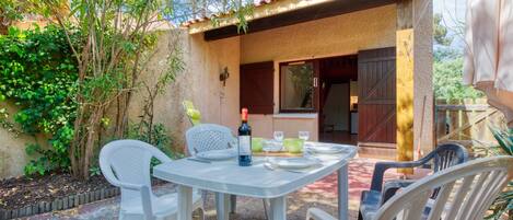 Une terrasse extérieure avec une table dressée pour deux personnes, entourée de chaises en plastique blanches.