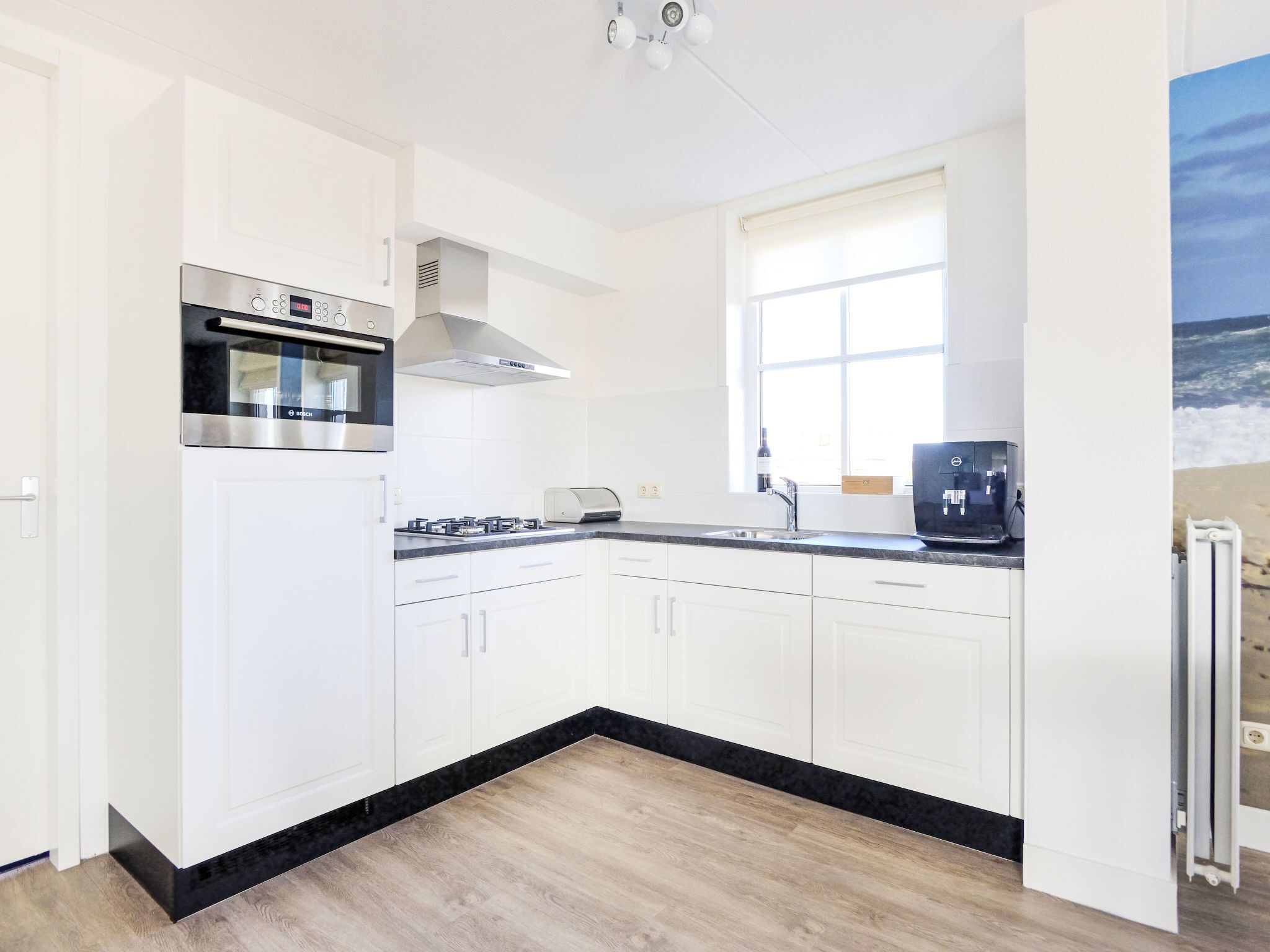 A modern kitchen with white cabinetry, a Bosch oven, a built-in stove, and a window providing natural light.