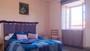 A bedroom with a bed, a chair, a nightstand, a lamp, and a window with curtains. - Vacation home ferme by Interhome (Puy-en-Velay)