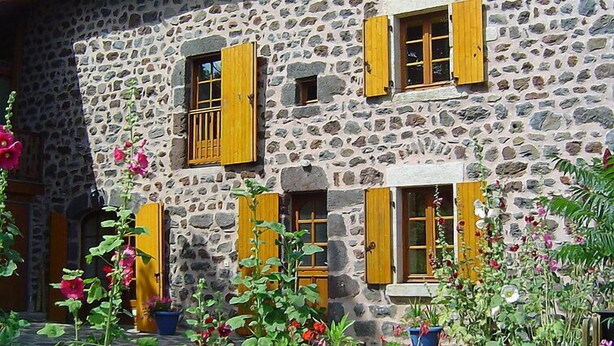 A stone building with multiple windows and doors, surrounded by potted plants and flowers. - Vacation home ferme by Interhome (Puy-en-Velay)