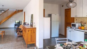 A spacious kitchen with a wooden dining area, a refrigerator, a microwave, and a dining table set with plates, bowls, and a kettle. - Vacation home ferme by Interhome (Puy-en-Velay)