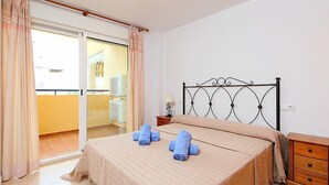 Ein Schlafzimmer mit Bett, Nachttisch, Lampe und Blick auf den Balkon.