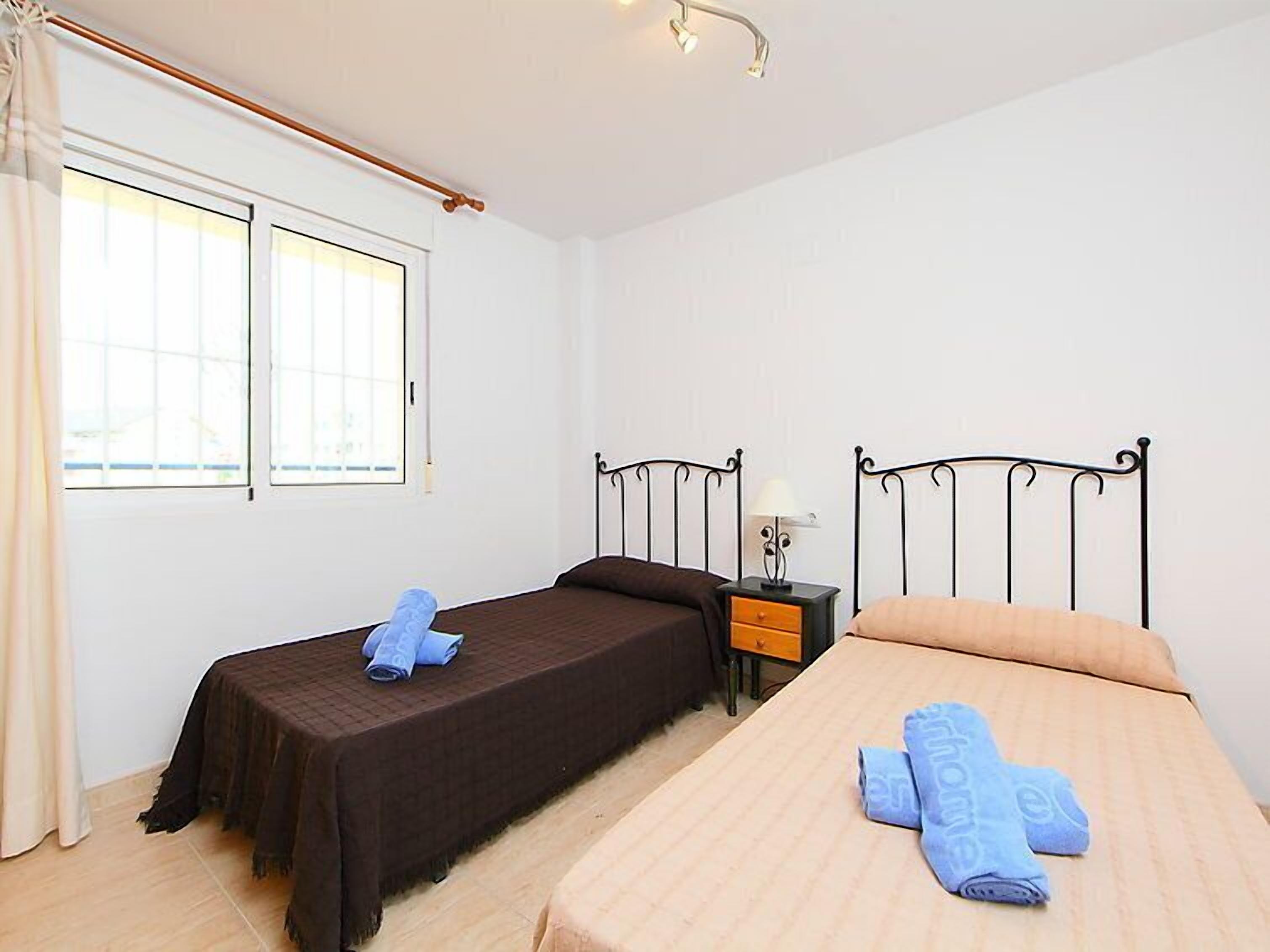 Una habitación con dos camas individuales, una mesita de noche con lámpara y una ventana con cortinas.