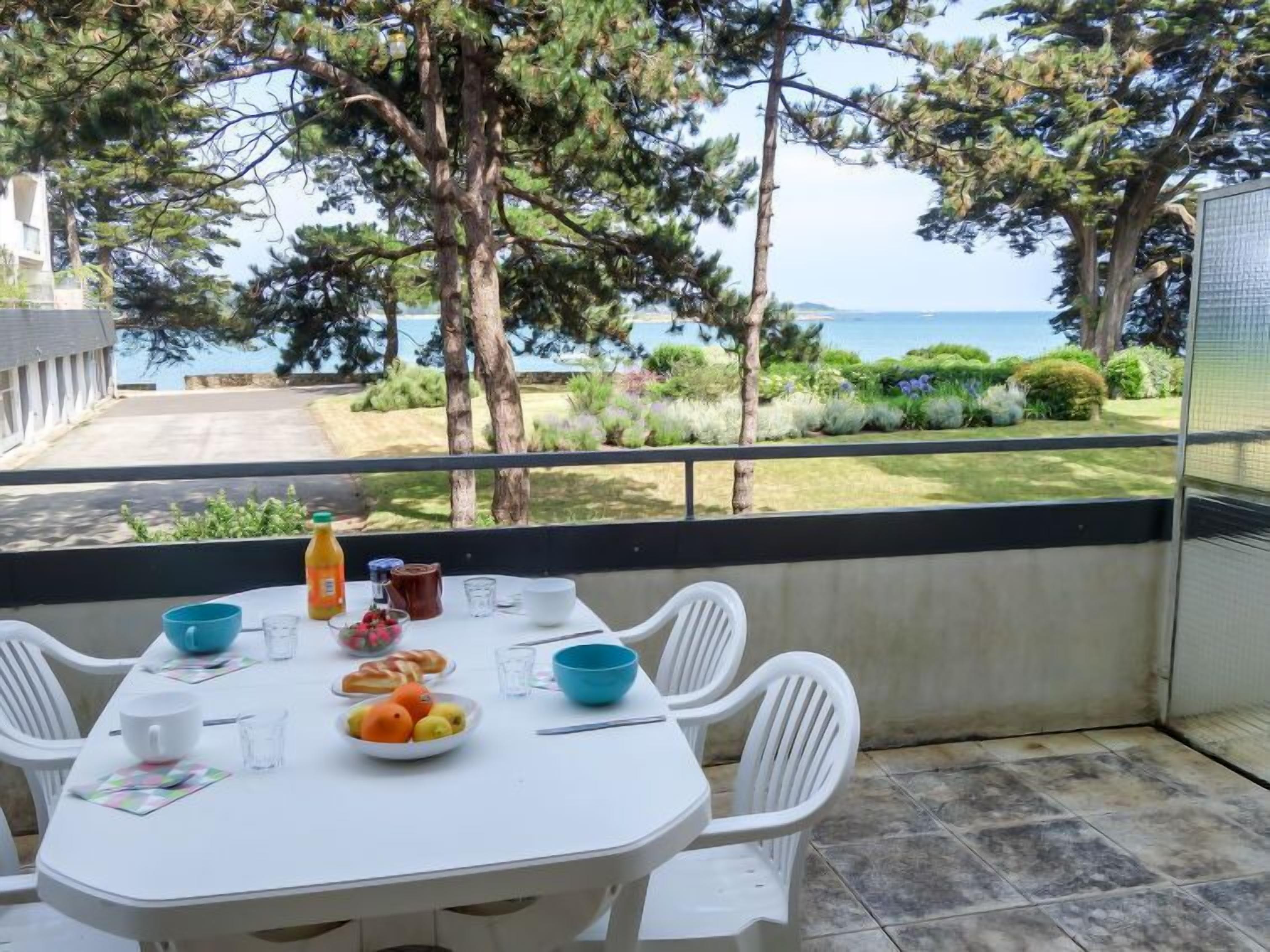 A dining area with a table set for two, overlooking a scenic view of the sea and greenery.