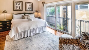 A bedroom with a bed, two bedside tables, a chair, a large window, and a balcony.