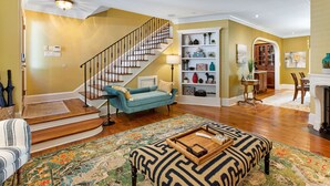 A spacious living room with a staircase, a blue sofa, a patterned rug, and a wooden coffee table.
