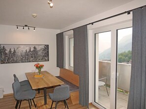 A modern room with a wooden dining table, two grey chairs, a vase with red flowers, a framed black and white painting, and a view of greenery and mountains through large windows. - Apartment Ladis by Interhome (Fiss)