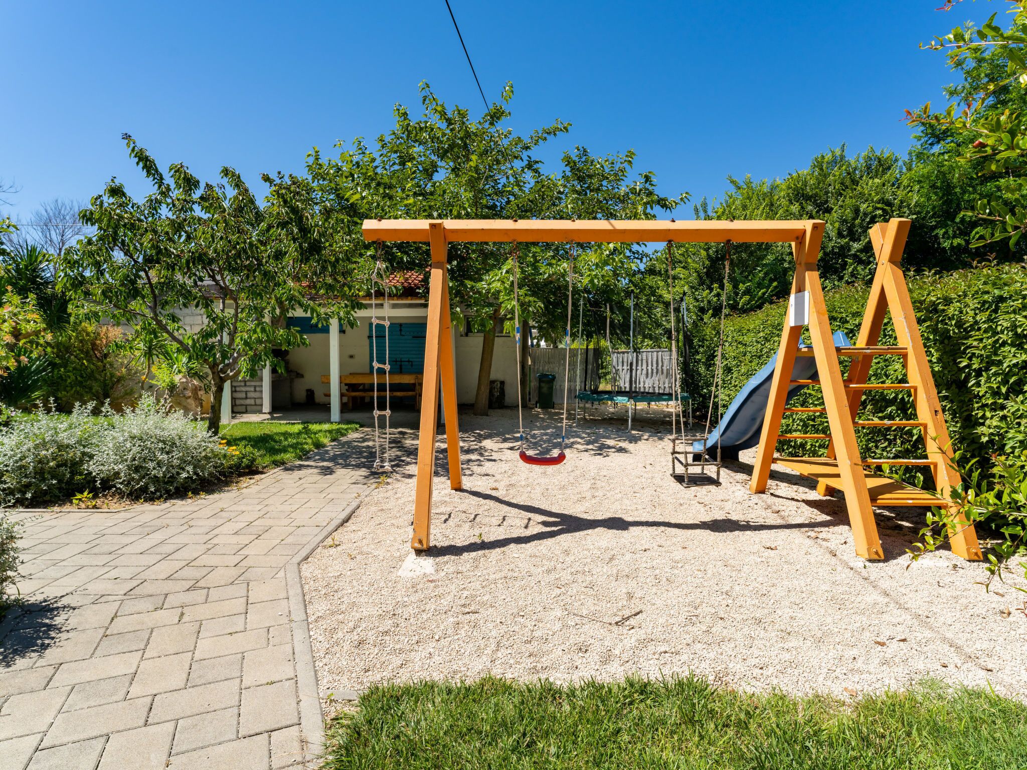 Un terrain de jeux avec des balançoires et un toboggan, entouré d’arbres et avec un bâtiment visible au loin.