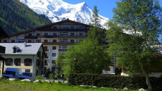 A multi-story hotel with a mountain backdrop, featuring balconies and a parking area. - Les Periades by Interhome (Chamonix)