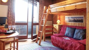 A cozy room with a bunk bed, a wooden desk with a chair, a table with a bottle and glasses, and a window with curtains. - Les Periades by Interhome (Chamonix)