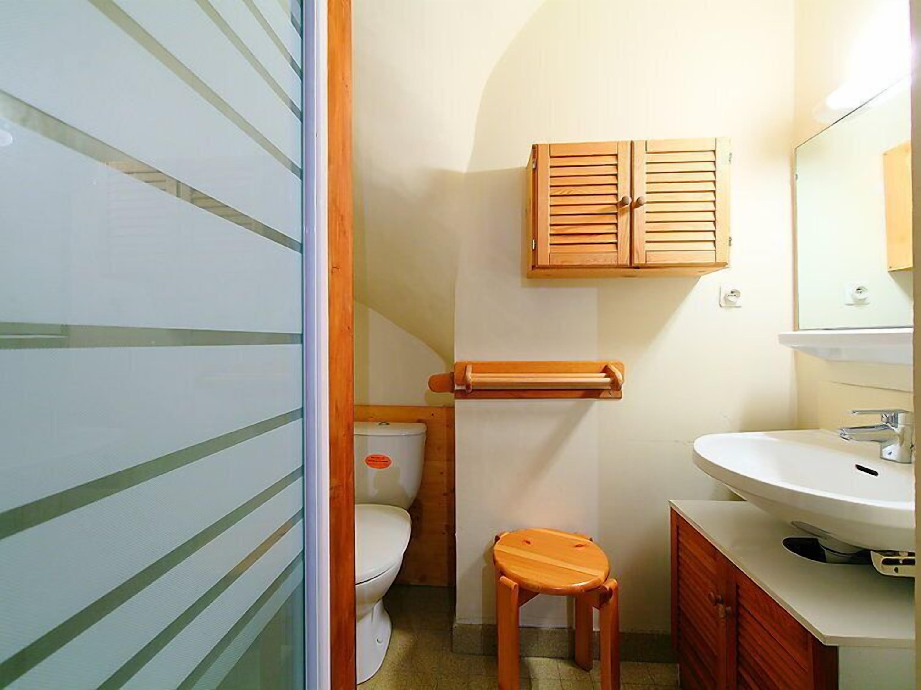 A compact bathroom with a toilet, wooden cabinet, and a sink.