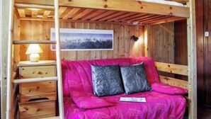 A wooden bunk bed with a pink patterned mattress, a small bedside table with a lamp, and a framed picture on the wall. - Les Periades by Interhome (Chamonix)