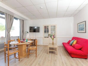 Una sala de estar con un sofá rojo, una mesa de comedor de madera, sillas, un televisor y una puerta con paneles de vidrio.