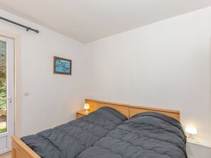 Quarto com cama, mesa de cabeceira com abajur, porta e quadro pendurado na parede.